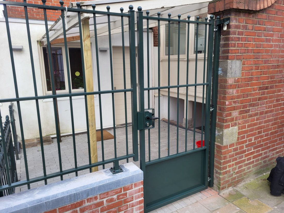 Groene stalen looppoort, halfdicht, naast een woning